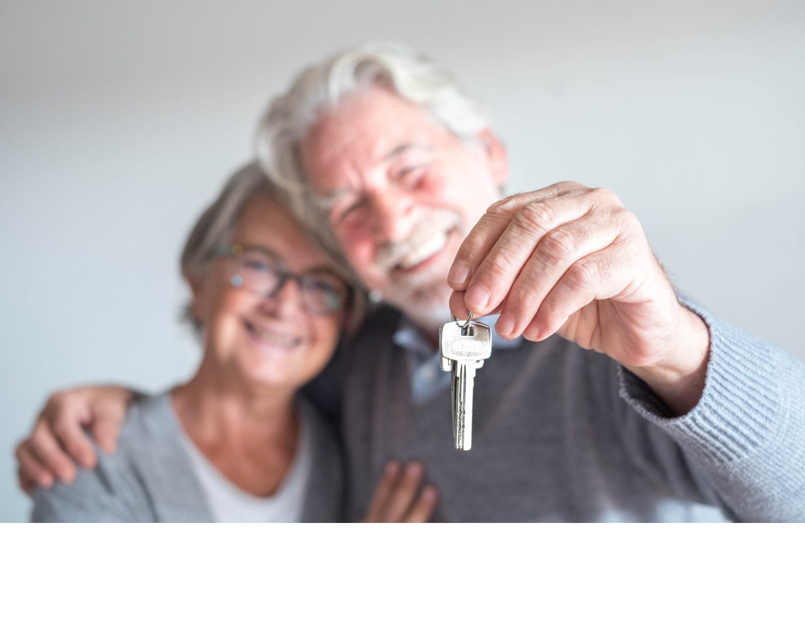 Happy older couple holding house keys and smiling after purchasing their new home.